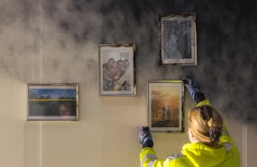 Opiskelija asettelee valokuvia seinälle, joka näyttää palaneelta