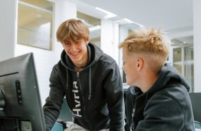 kaksi nuorta Hyrian huppareissa tietokoneen ääressä