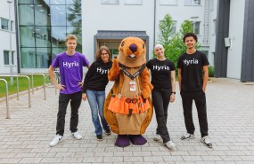 Kuva jossa nuoret seisovat rivissä hymyillen, yhdessä Hyrian Majava maskotin kanssa.