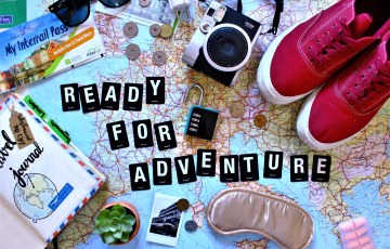 Kartan päälle sommiteltu tennarit, kamera, opas, silmämaskit ym ja teksti Ready for Adventure.