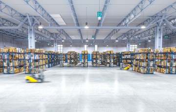 Valokuva suuresta varastosta, jossa on kaksi liikkuvaa trukkia. 