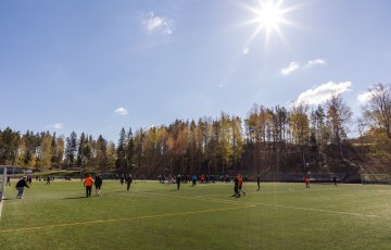 Valokuva jalkapallokentästä. Kentällä on pelaajia ja aurinko paistaa.