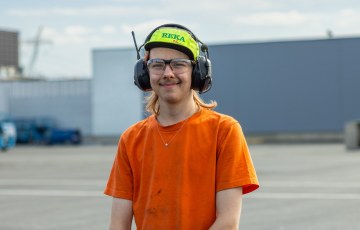 Puolivartalokuva jutussa esiintyvästä Juhosta. Juholla on yllään sähköasentajan työvaatteet. Juho hymyilee.