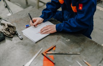 Kuvituskuva. Valokuvassa henkilö kirjoittaa paperille. 