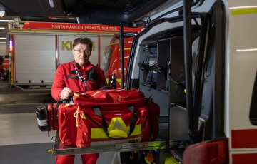 Henkilö esittelee ambulanssin tarvikelaukkua ajoneuvohallissa.