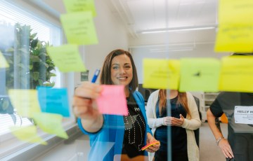 Anna Skytten laittaa toimistotilassa post-it lappua lasiseinään kiinni. 