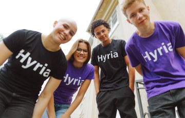 Neljä nuorta katsoo alaspäin kohti sinua ja he hymyilevät.