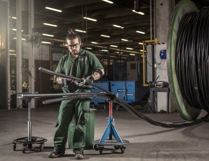 Kaapelityöntekijä testaa kaapelia Rekan Riihimäen tehtaalla, taustalla iso kaapelikela.