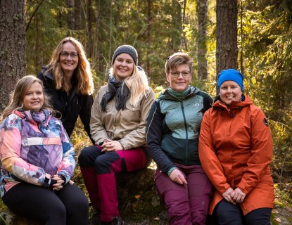 Viisi henkilöä istumassa kivellä metsässä