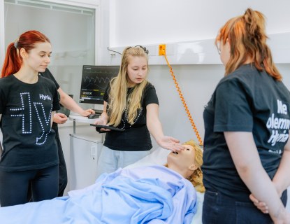 Lähihoitajaopiskelijat hoitoluokassa hoitamassa hoitonukkea.